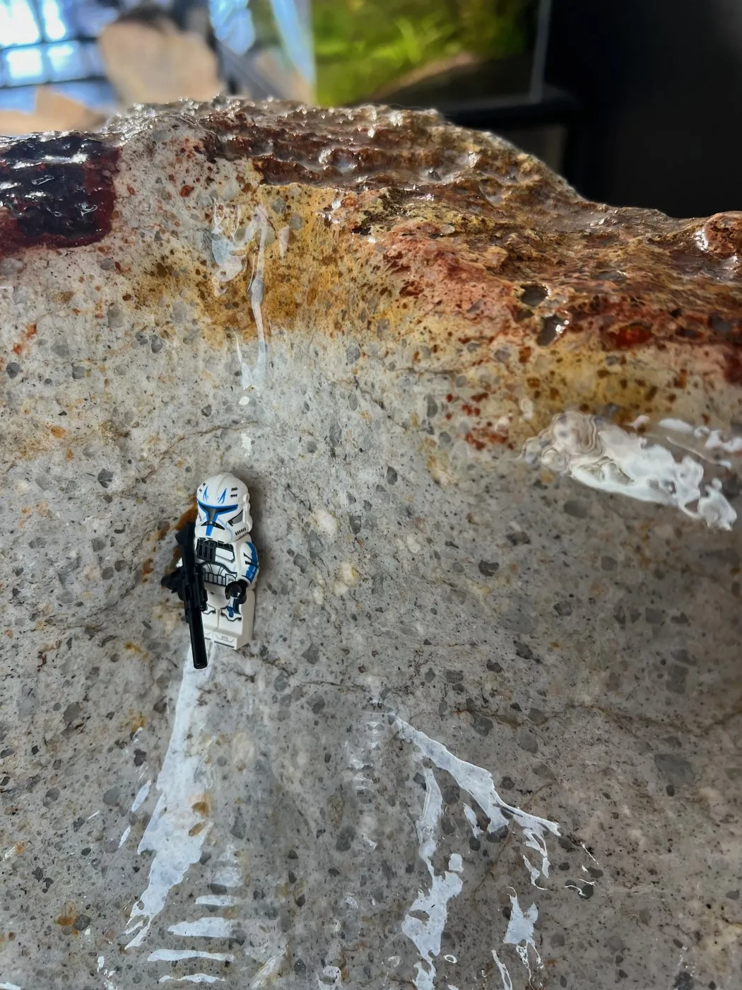 Inside the carved bowl of Iron Fen #03: speckled grey quartz monzonite below the iron-stained red rim, with a toy figure for scale